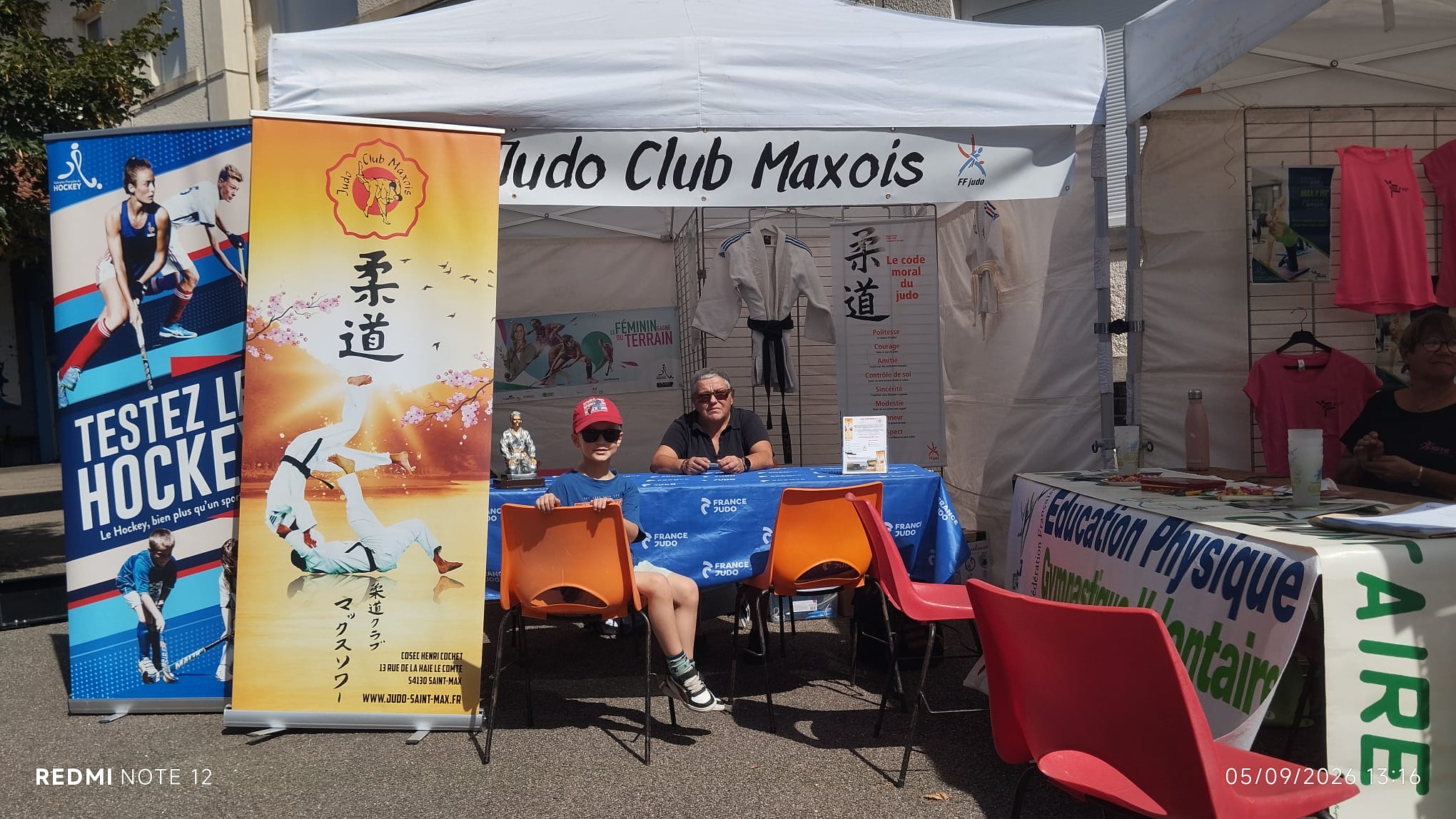 Le stand du Judo Club Maxois sous un barnum : banderole du club, judogi exposé, affiche du code moral du judo et table France Judo