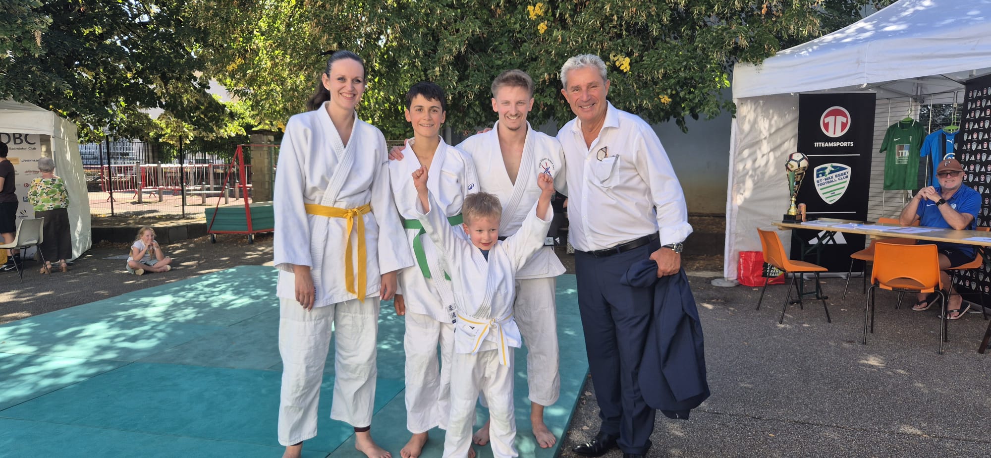 Quatre judokas en judogi posant avec Éric Pensalfini, maire de Saint-Max, devant les stands du forum